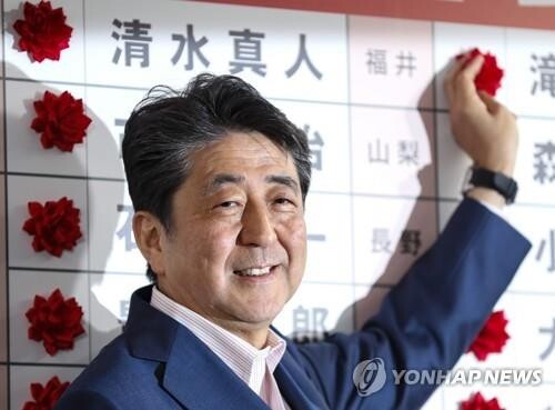 아베 신조 일본 총리가 21일 치러진 참의원 선거의 자민당 당선자 이름에 꽃을 달고 있다. [사진= EPA/연합뉴스]